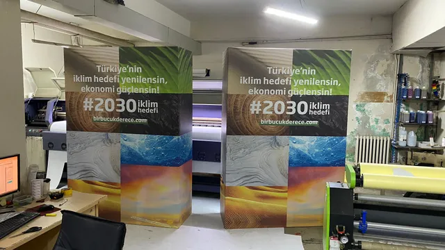 İklim hedefi panoları — atölye — 2030 iklim hedefi mesajını taşıyan iki baskılı panonun atölyedeki hazırlık görünümü.