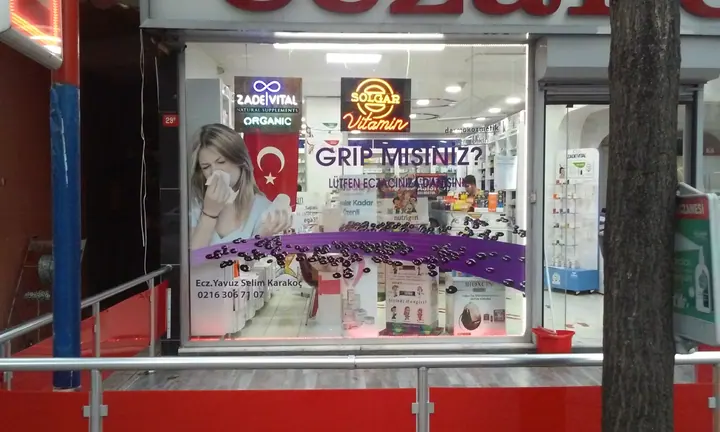 Alaçay Eczanesi kampanya vitrini — Cam yüzeyde kampanya görseli ve kesimli grafiklerin görünümü.